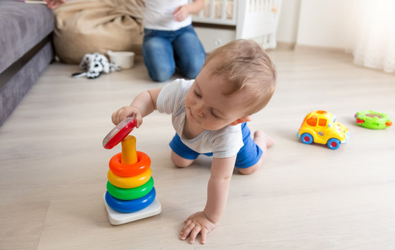 Adorable baby crawling on floor and assembling colorful toy towe
