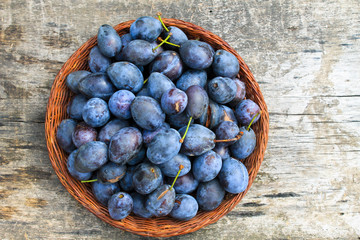 Fresh plums in rustic bowl on old wooden background