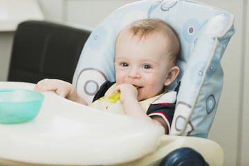 Toned portrait of smiling baby sitting in highchair and eating g