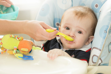 Closeup of baby boy sitting behind table at highchair and eating