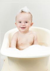 Cheerful laughing 9 months old baby playing in foam at bath