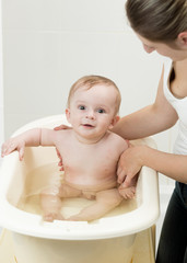 Mother bathing her adorable baby in bathroom