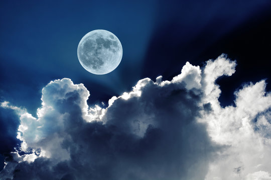 Big full moon in night sky with beautiful white clouds glowing in the moonlight