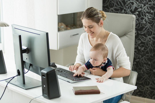 Smiling businesswoman working at computer with baby boy sitting