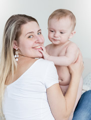 Happy young mother sitting on bed and holding her 9 months old b