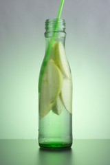 Green bottle with natural apple lemonade on the table. Slices of green apple in a bottle with a straw.