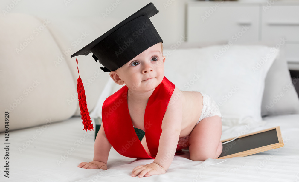 Wall mural adorable 10 months old baby in graduation cap crawling on bed