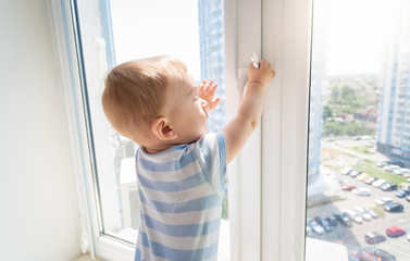 Baby in danger. Baby pulling handle of window