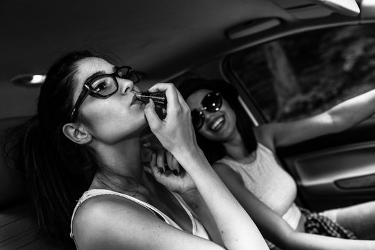 Two young women inside the car.They are driving the car and fixing makeup.Preparing to go out.Clubbing and nightlife.
