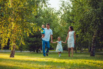 Naklejka na ściany i meble Happy young family of four people walking and having fun in the park