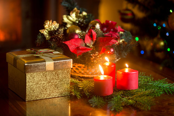 Burning candles by the decorated Christmas tree, giftbox and tra