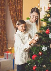 Teenage girl helping mother decorating Christmas tree