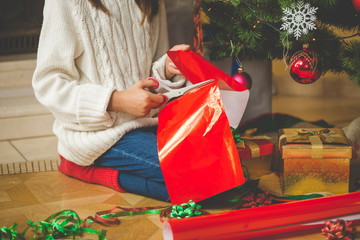 Fototapeta premium Closeup of girl sitting under Christmas tree and cutting red pap