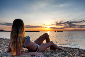 Fototapeta na wymiar attractive sexy woman in bikini laying on sand on lonely beach on sunset sunrise