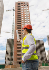 Rear view of architect pointing with blueprints at building unde