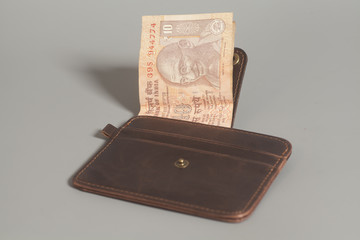 Brown leather wallet with Indian rupee currency on gray backgrou