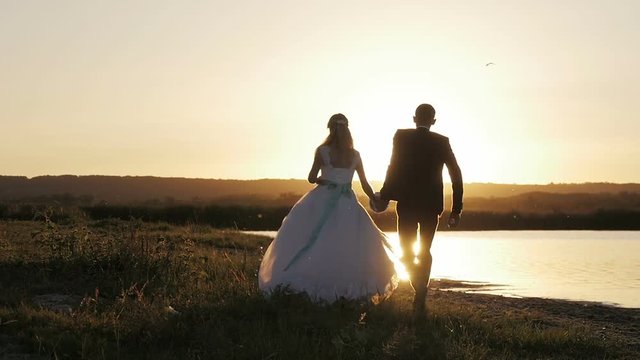 bride and groom running through the field to meet the sun at sunset, slow motion