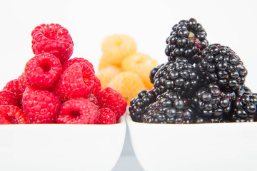 Raspberries and blackberries: bowls of fruit on white background