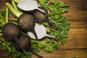 Black radish and leaves on the background of wooden boards