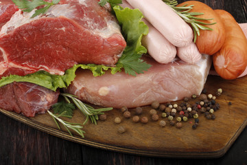 meat and sausages with vegetables and spices on wooden background
