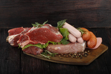 meat and sausages with vegetables and spices on wooden background