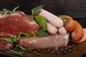 meat and sausages with vegetables and spices on wooden background