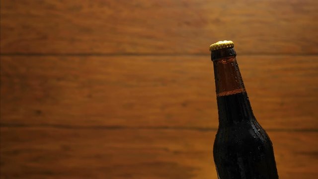Cold bottle of beer on wood broun background. Drop flows down the bottle