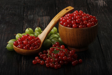 red currant and gooseberry in wooden plate on wooden background