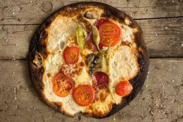 Burnt pizza with tomatoes, salami,pepperoni on wooden rustic background Overhead view