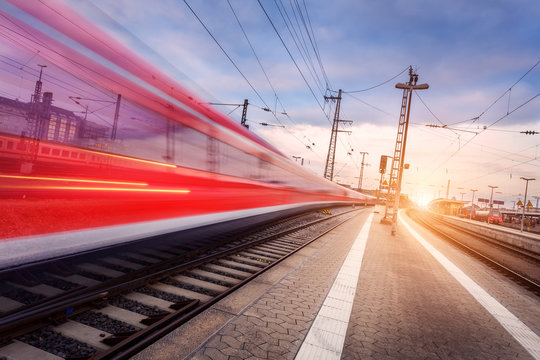 Fototapeta High speed red passenger train on railroad track in motion at beautiful sunset. Blurred commuter train. Railway station in the evening. Railroad travel, railway tourism. Industrial landscape. Train