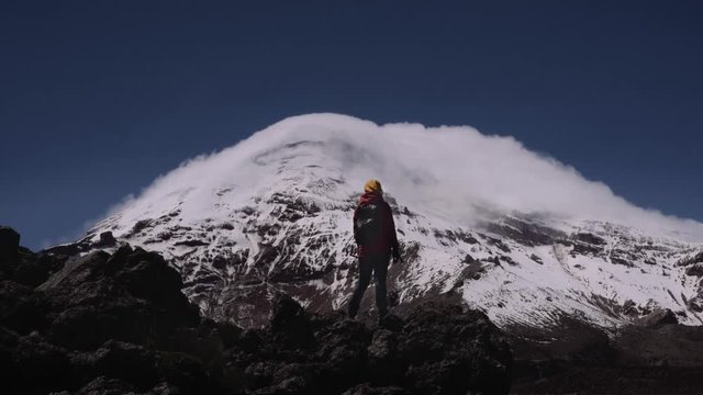 Female hiker on the peak of mountain contemplating the marvelous view of the snow peak of the Chimborazo Volcano in Ecuador.