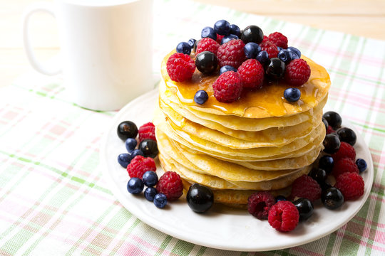 Breakfast pancakes with honey and fresh berries on the white pla