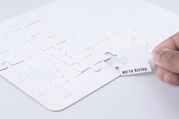 Closeup of businesspeople about to put four puzzle pieces with we're hiring word