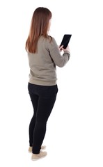 Fototapeta premium back view of standing young beautiful woman using a mobile phone. girl watching. girl in a gray sweater standing sideways and read e-books.