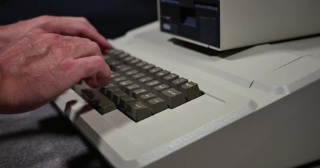 Profile shot of someone typing on an old-style 1980s personal computer. Shallow depth of field.	 	