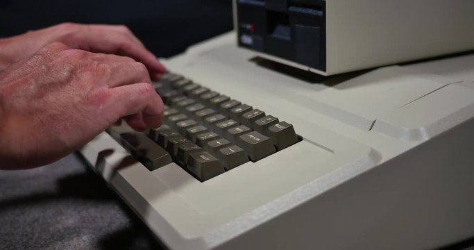 Profile shot of someone typing on an old-style 1980s personal computer. Shallow depth of field.	 	