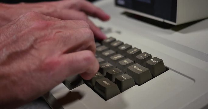 Close profile shot of someone typing on an old-style 1980s personal computer. Shallow depth of field.	 	