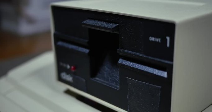 Close-up shot of someone inserting and removing an old-style 5.25-inch floppy disk.	Shallow depth of field.  	