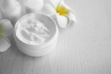 Fototapeta na wymiar Facial cream and exotic flowers on white wooden background