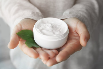 Woman holding jar with cream and green leaves, closeup