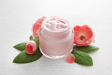 Facial cream and pink flowers on white wooden background