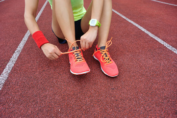 young woman runner tying shoelaces on tracks