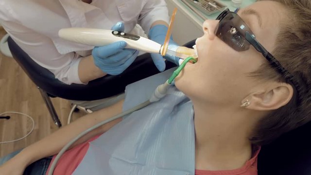 Woman at dentist clinic gets dental treatment to fill a cavity in a tooth. Dental restoration and material polymerization with UV light. Odontic and mouth health is real protection from caries decay.