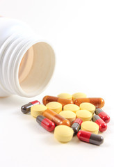 Pile of pills and white bottle isolated on white background.