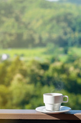 White cup of hot coffee on balcony with natural and mountains.