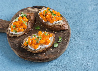 Pumpkin and goat's cheese bruschetta on a wooden cutting board on blue background. Healthy vegetarian snack