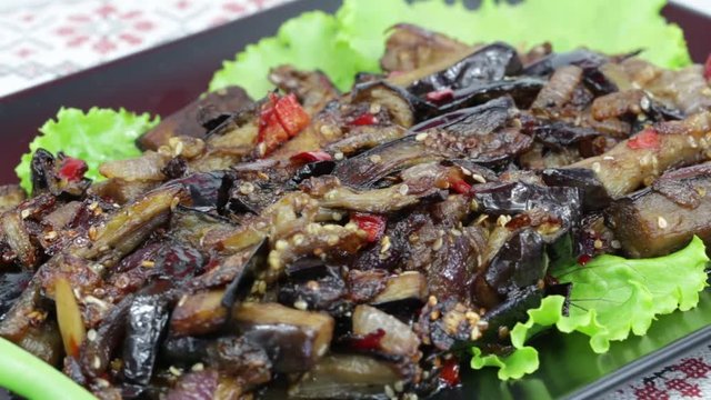 Baked eggplant with onions, garlic, red hot chili pepper and walnuts on the black plate, close up