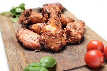 Fried chicken wings on rustic serving board, spicy tomato sauce, herbs and mug of light beer over white backdrop, top view