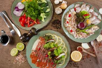 Different vegetables, meat, red fish and other dishes, sauces, snacks and spices on a wooden background