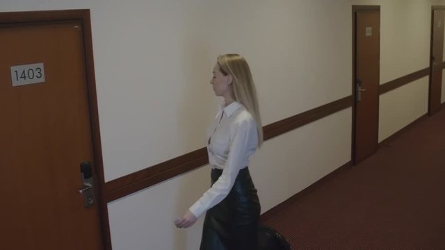 Tracking of confident young businesswoman going down hallway with suitcase and then entering her hotel room